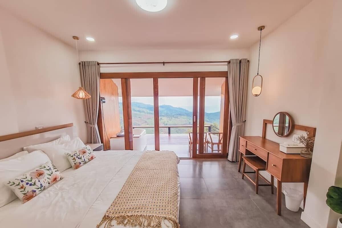 A bedroom with a bed, a desk, and a view of the outdoors.