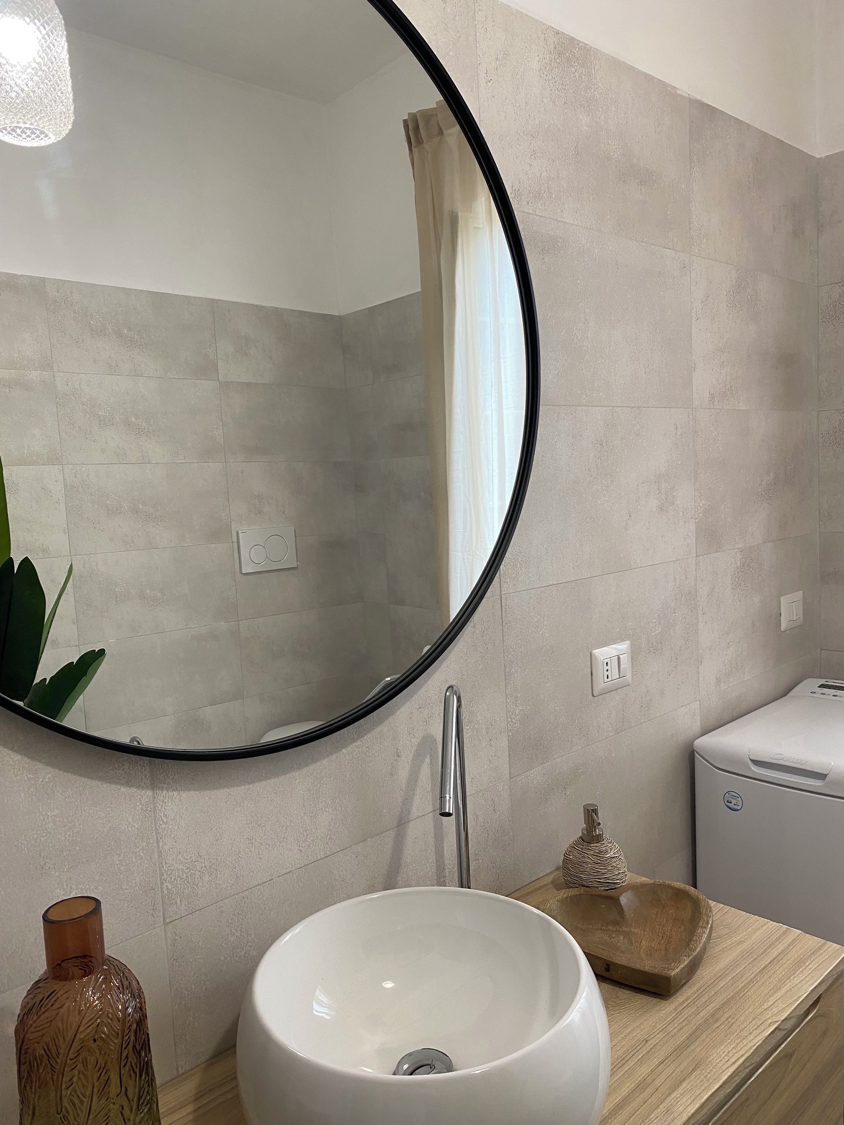 A bathroom with a round mirror, a white sink, a wooden tray, and a towel rack.