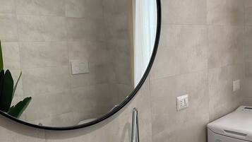A bathroom with a round mirror, a white sink, a wooden tray, and a towel rack.