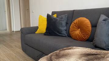 Un salon moderne avec un canapé gris, un plaid marron à poils longs et divers coussins.
