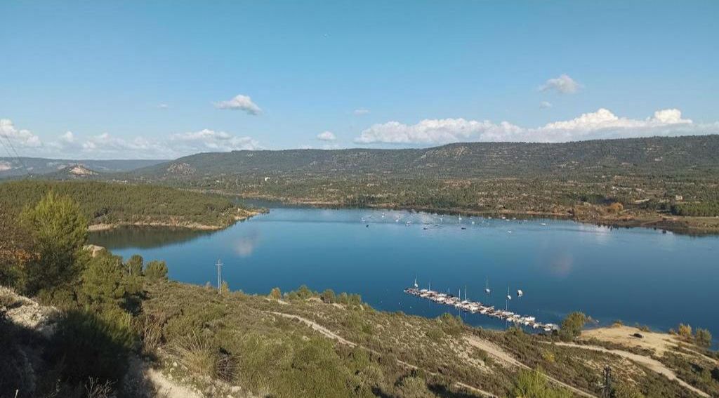 Un llac amb barques, envoltat de turons i vegetació escassa.