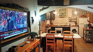 A cozy kitchen with a dining area, a TV displaying a news broadcast, and a brick wall.