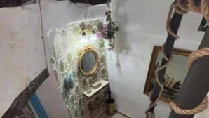 A narrow staircase with a patterned floor, a small alcove with a mirror and decorative items, and a stone wall with a floral design.