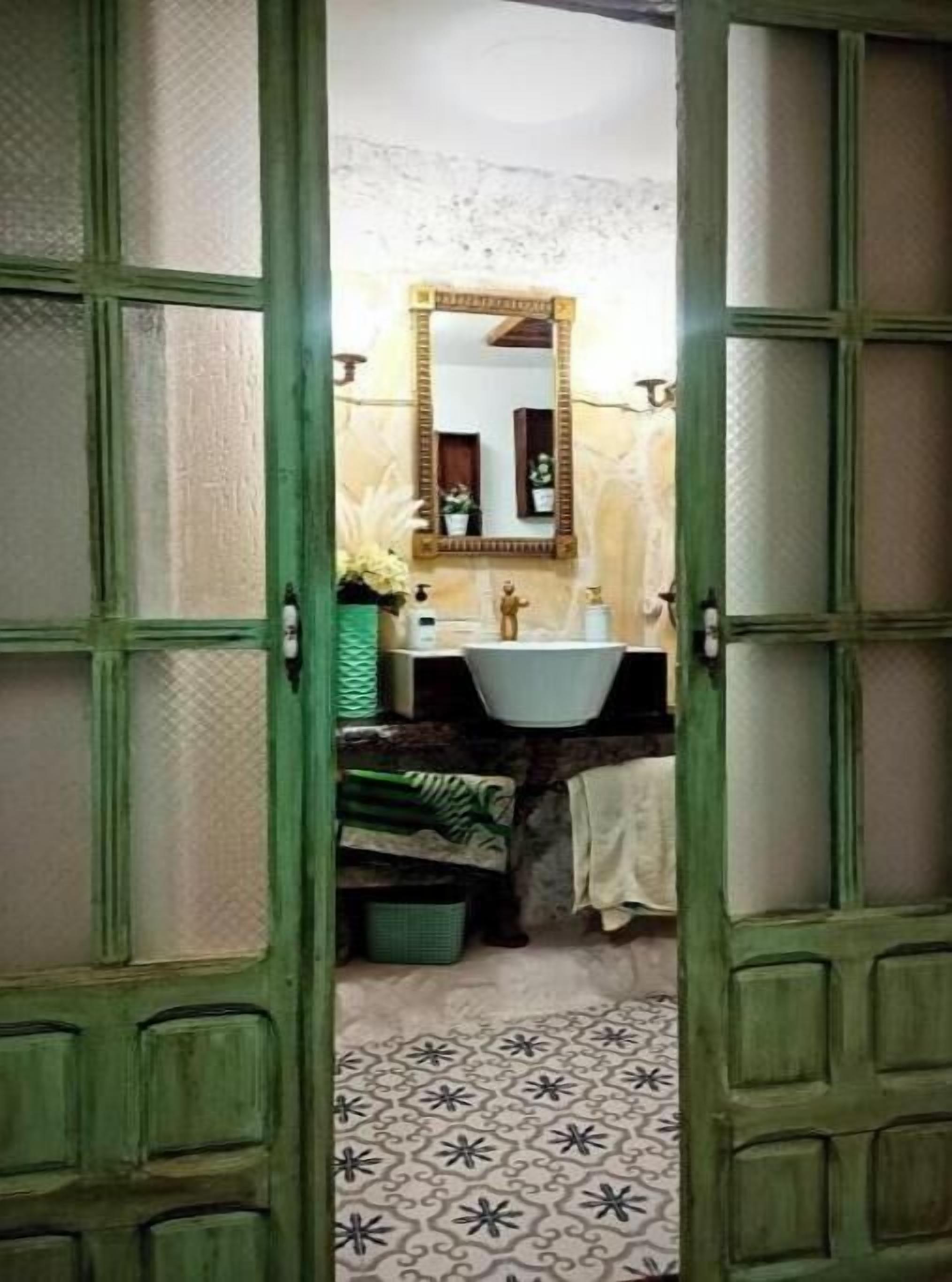 A bathroom with a green door, a white sink, a mirror, and a patterned floor.