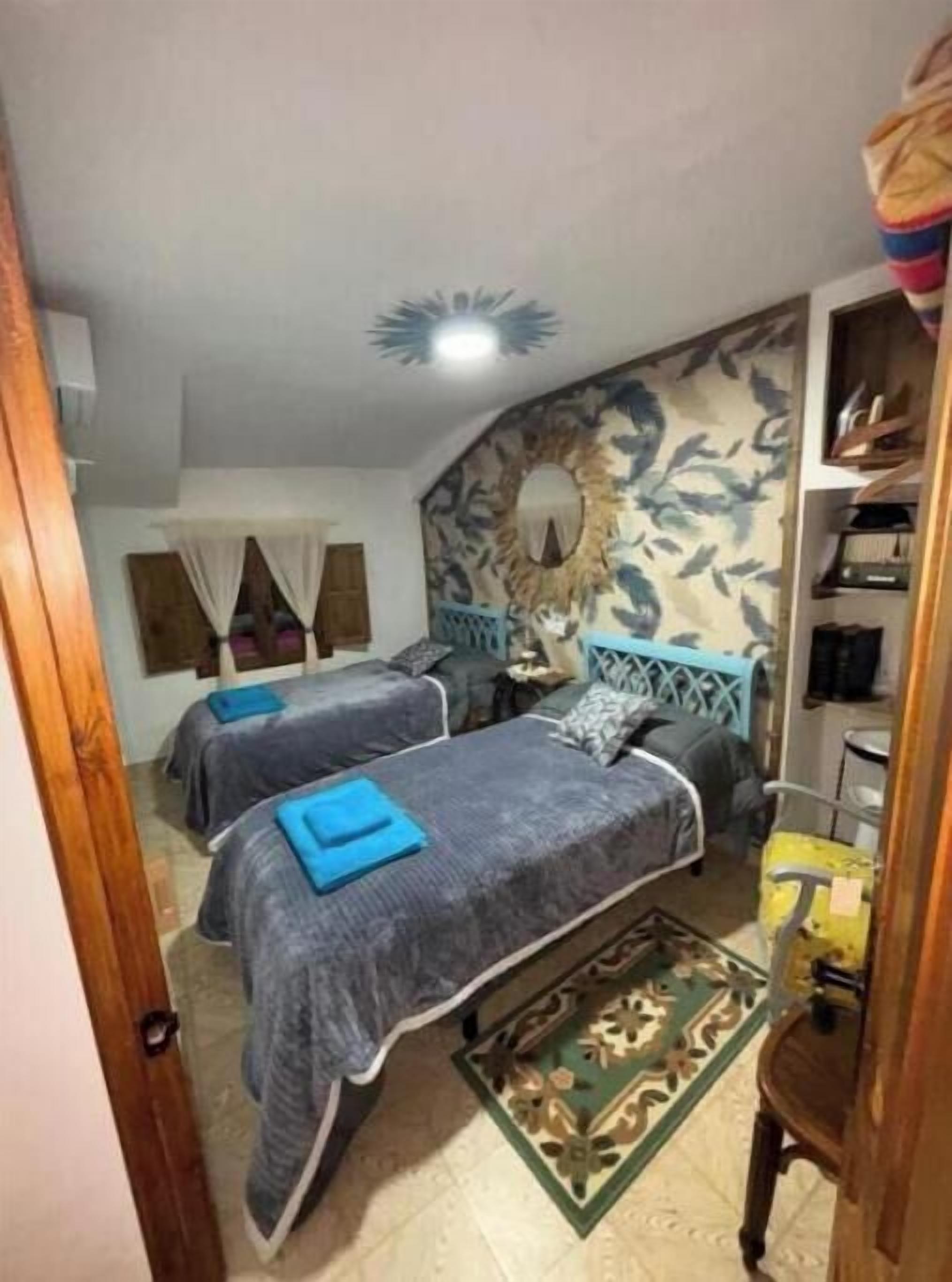 A room with two beds, a decorative wall, a wooden cabinet, and a patterned rug.