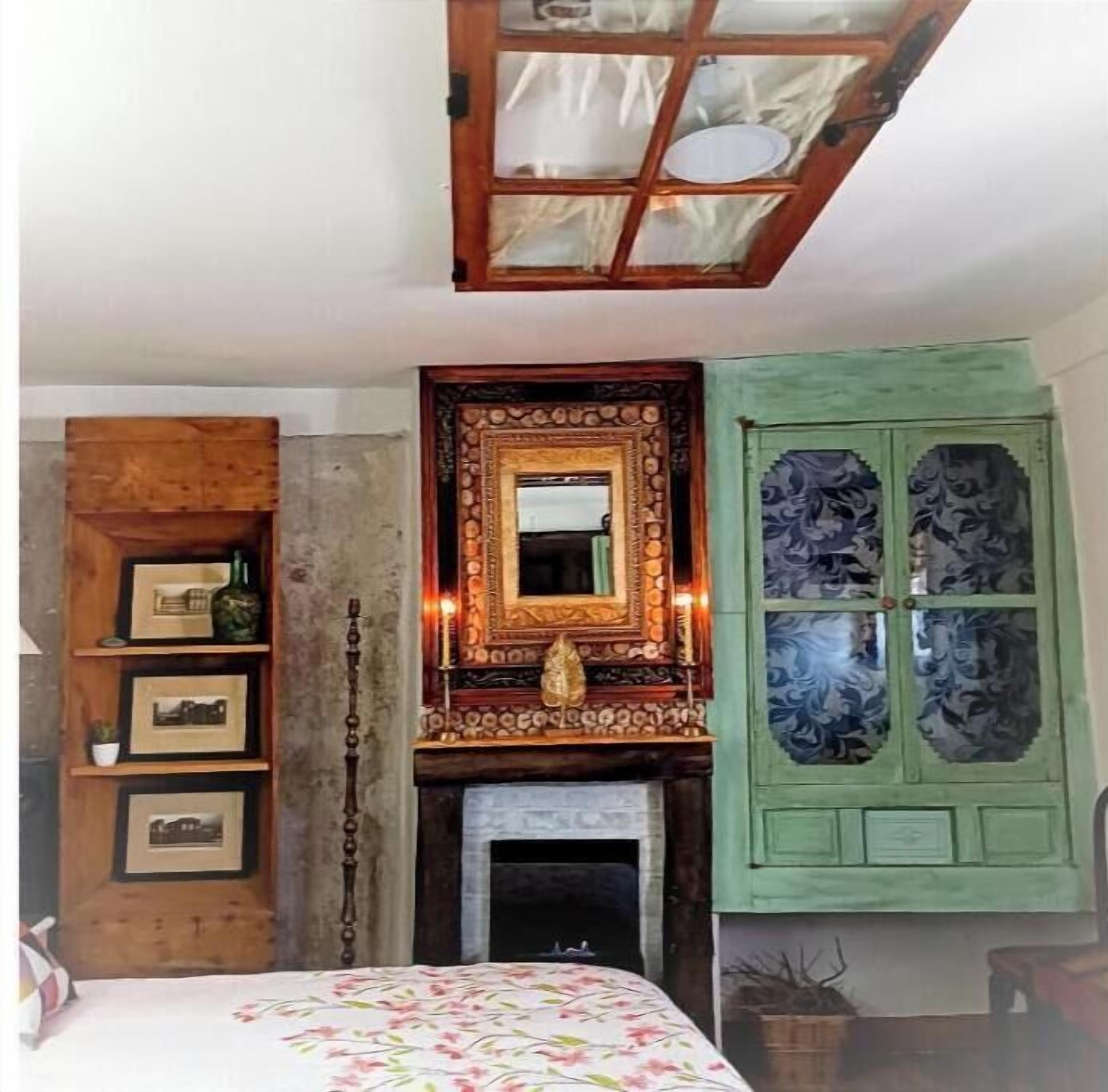 Una stanza con camino, uno specchio con cornice decorata e un mobiletto verde con pannelli di vetro decorativi.