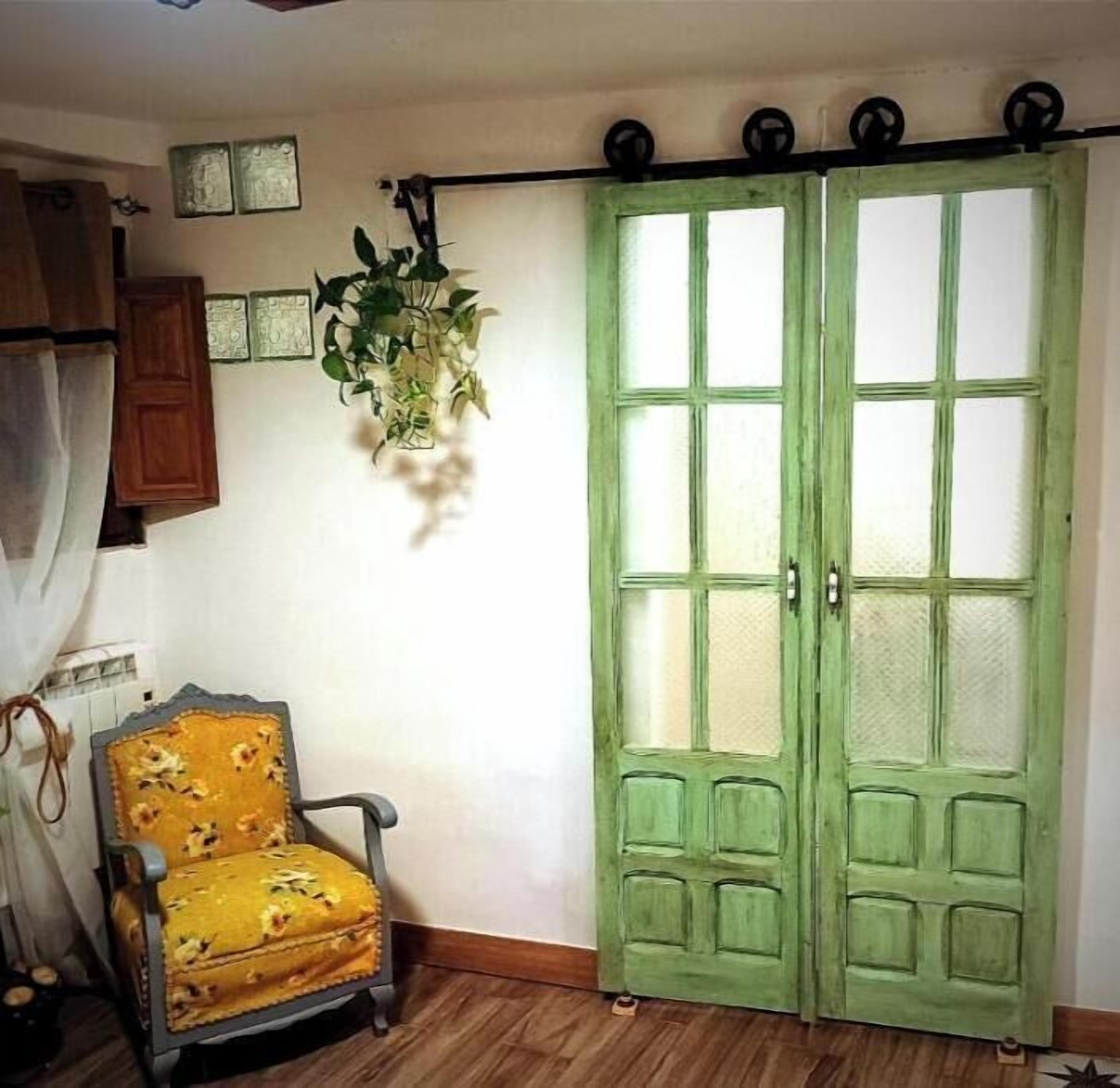 Une pièce avec une porte verte, un fauteuil jaune et une plante accrochée au mur.
