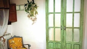 Une pièce avec une porte verte, un fauteuil jaune et une plante accrochée au mur.
