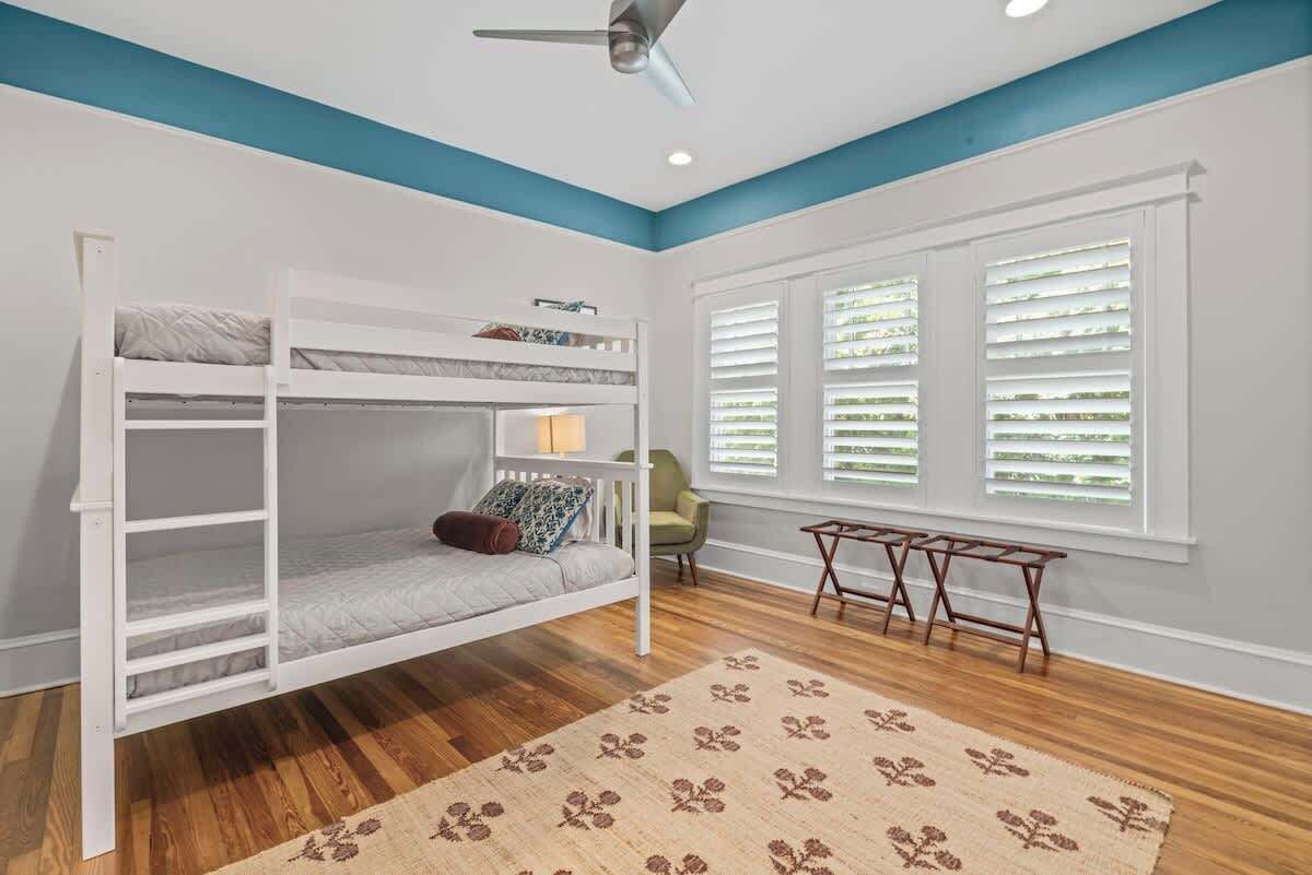 A room with a bunk bed, a small table, a chair, and a window with blinds.