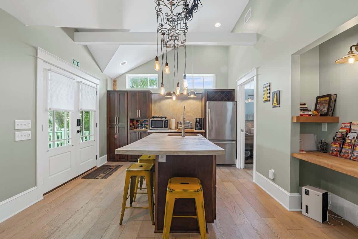 A modern kitchen with a central island, bar stools, a stainless steel refrigerator, and a hanging light fixture.
