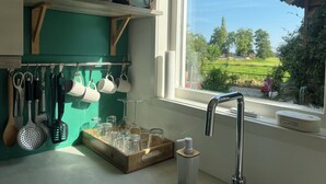 Ett kök med fönsterutsikt, köksredskap som hänger på väggen och ett bricka med glas.