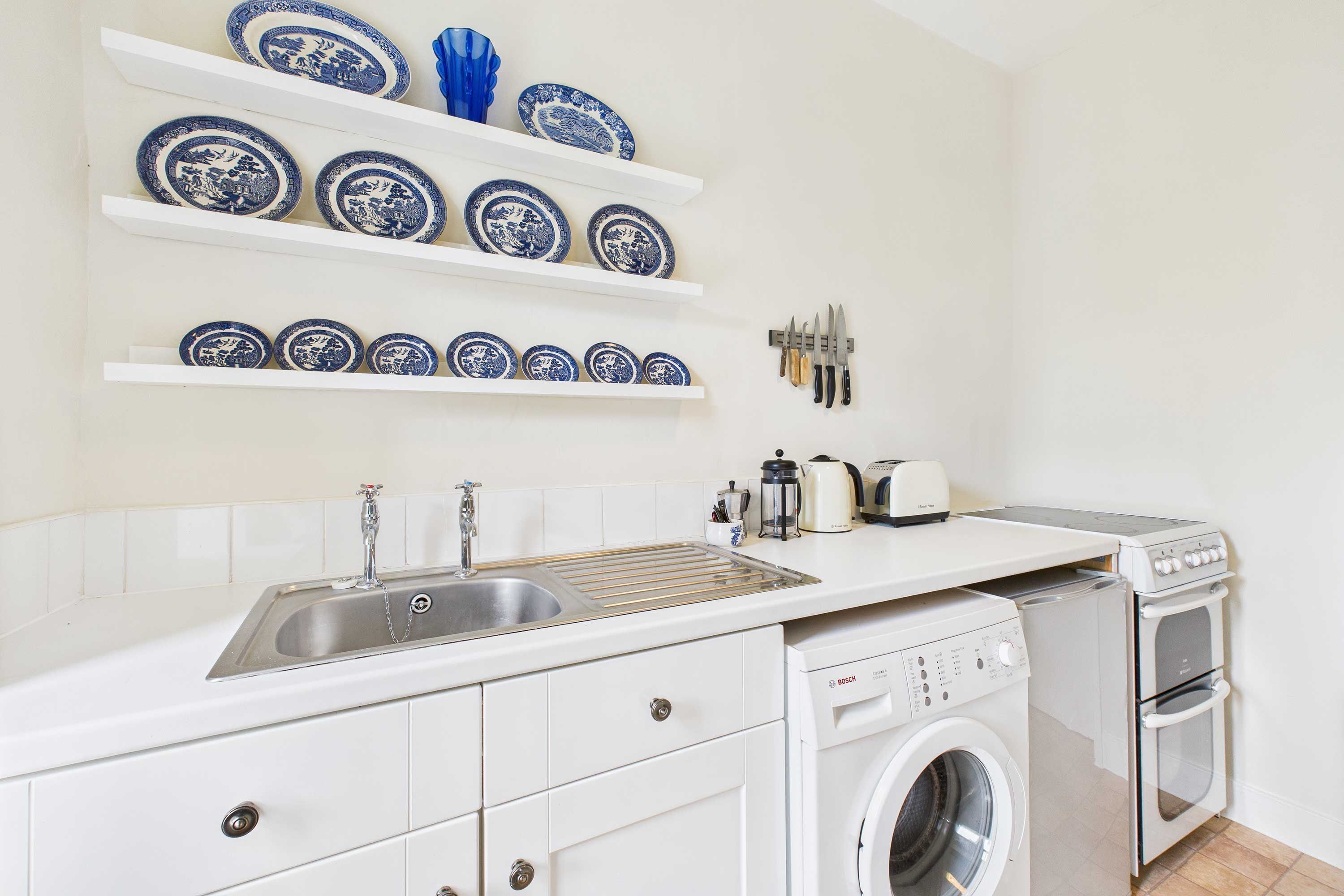 A kitchen with a sink, dishwasher, oven, and shelves with blue and white plates.