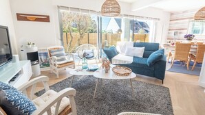 Un saló modern amb un sofà blau, cadires blanques, un moble de televisió de vidre i una finestra gran amb vistes a l'exterior.