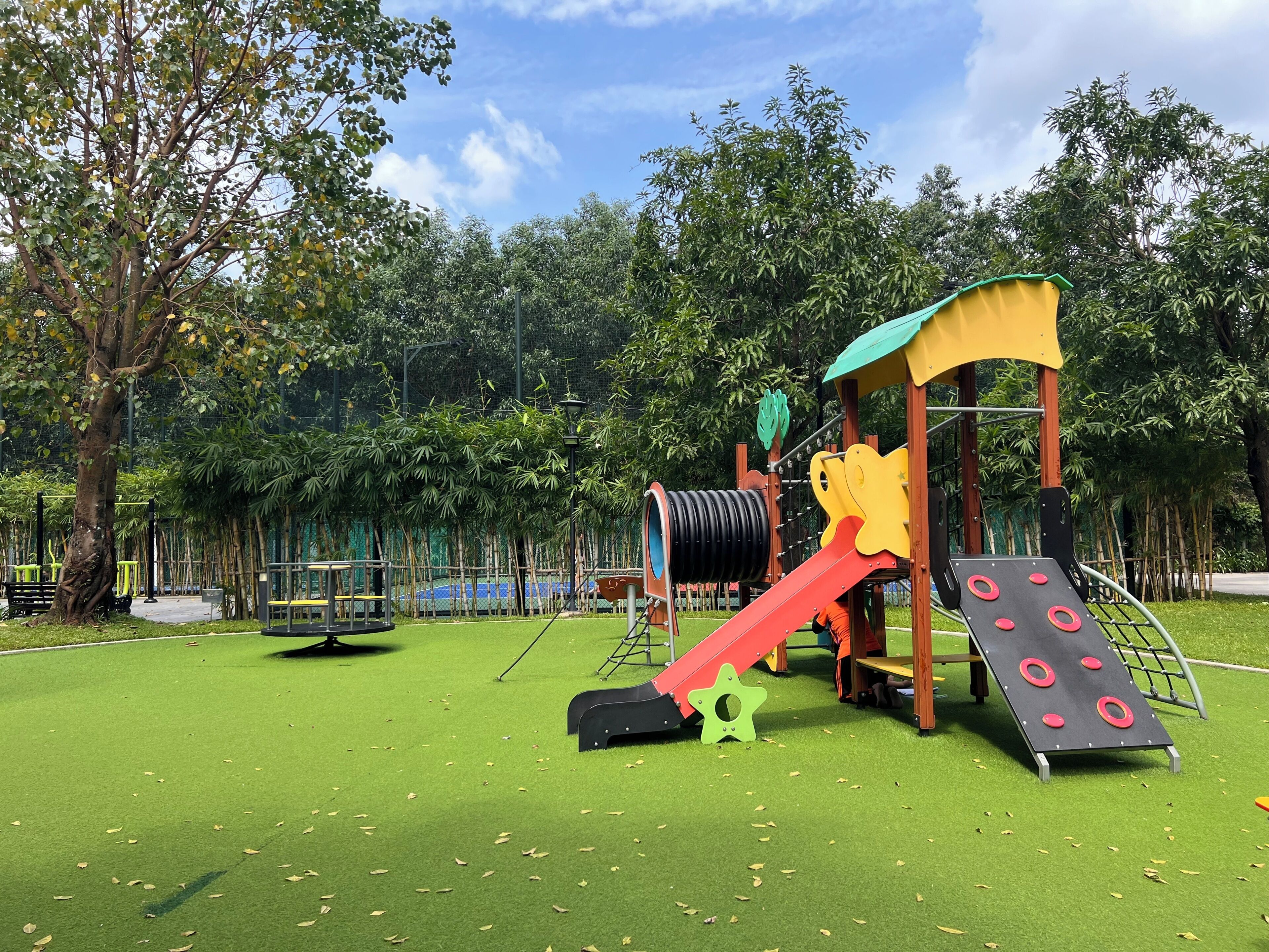 Un parque infantil con tobogán, red de escalada y estructura verde para trepar.