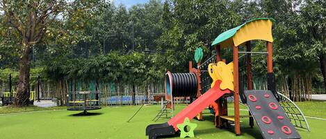 Un parque infantil con tobogán, red de escalada y estructura verde para trepar.