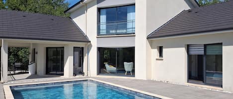 A modern two-story house with a swimming pool, large windows, and a covered patio area.