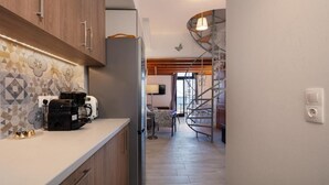 A modern kitchen with wooden cabinets, a coffee machine, and a spiral staircase leading to a living area with a sofa and a lamp.