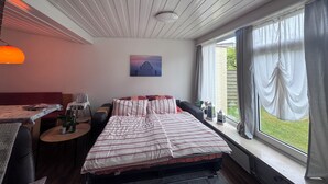 Ein Schlafzimmer mit Bett, Schreibtisch, Stuhl, einem Fenster mit Vorhängen und einem Bild an der Wand.