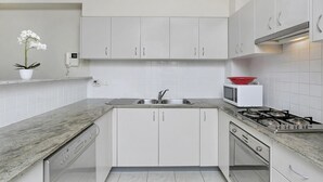 Una cocina moderna con armarios blancos, un lavamanos de acero inoxidable, un tazón rojo sobre un microondas y una estufa a gas.