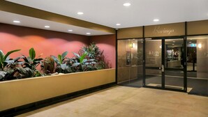 Entrada de hotel con diseño moderno, que incluye una puerta de cristal, un mostrador de recepción y una pared vegetal.