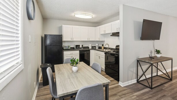 A modern kitchen with white cabinets, a black refrigerator, and a dining area with a wooden table and chairs.
