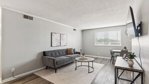 A modern living room with a grey sofa, a round coffee table, and a dining area with a table and chairs.