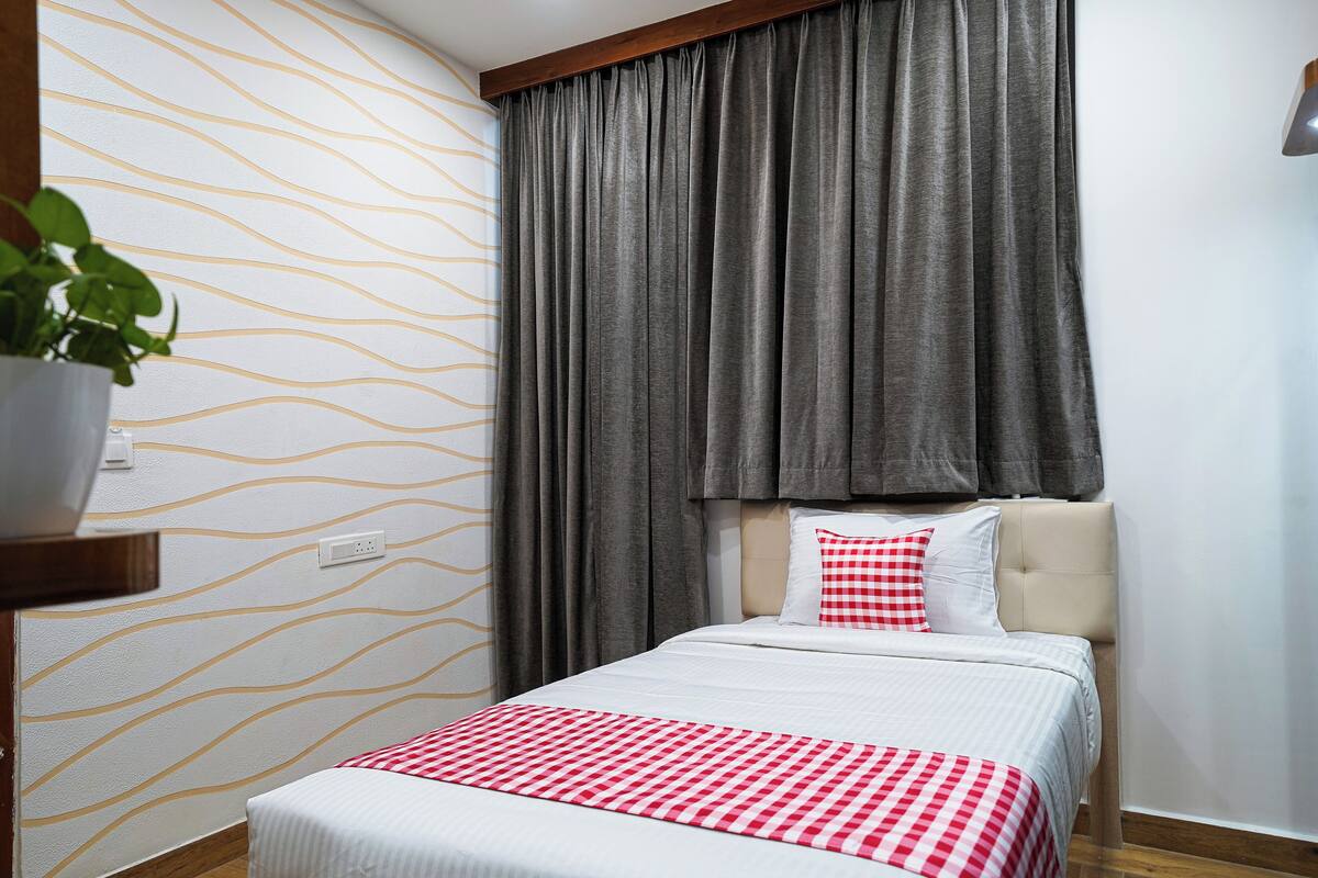 Une chambre d’hôtel avec un lit, une fenêtre avec des rideaux, un mur orné d’un motif ondulé et une plante en pot.