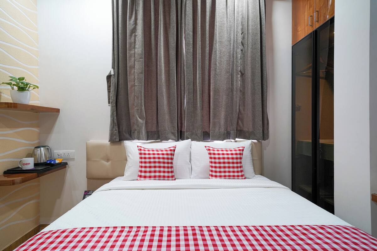 Une chambre d’hôtel avec un lit, une table de chevet, une plante et une fenêtre avec des rideaux.