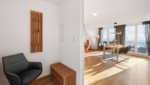 A modern living room with a black chair, a wooden slat wall art piece, and a dining area with a table and chairs. - Comfort kisses nature Skyline vacation apartment Goldbach (Goldbach)