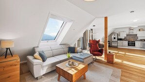 A modern loft apartment with a sloped ceiling, a sofa, a wooden coffee table, a red armchair, and a kitchen area. - Comfort kisses nature Skyline vacation apartment Goldbach (Goldbach)