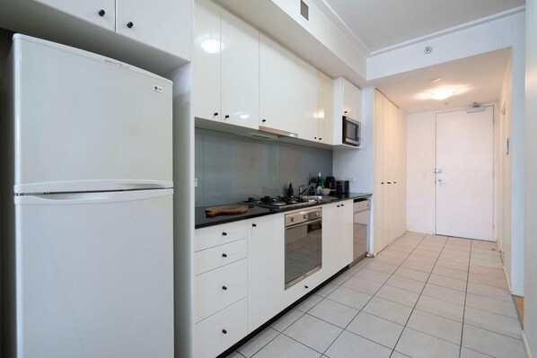 A modern kitchen with white cabinetry, a built-in microwave, a gas stove, and a refrigerator. - Sydney - KS004 - Kent St - CBD crib | Skyline views meet pool & gym living (Sydney)