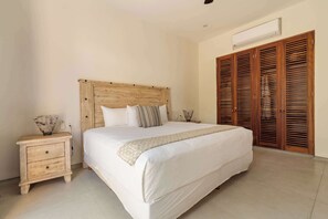 Un dormitorio con cabecera de madera, una cama grande, una mesita de noche con lámpara y un armario de madera.