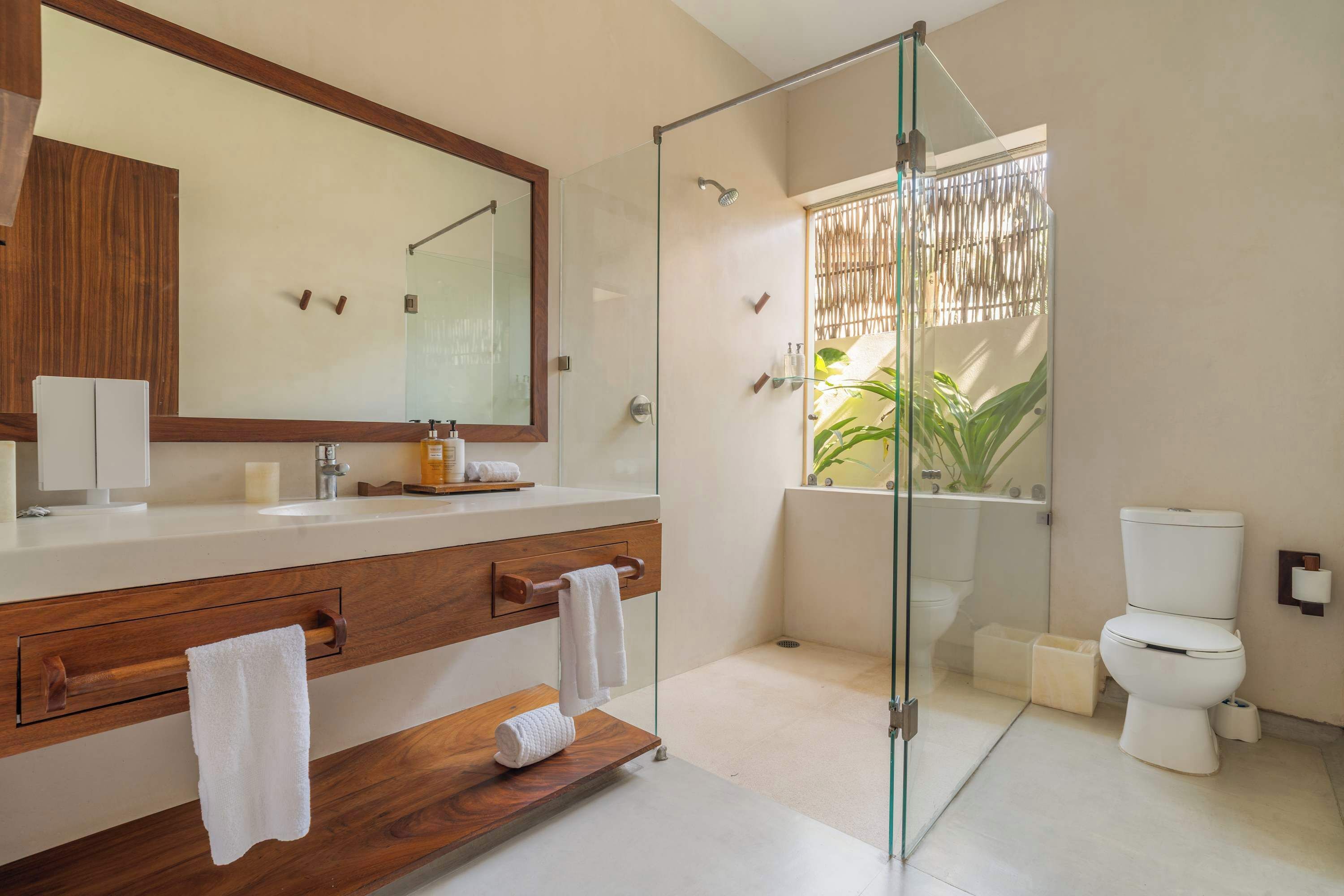 A modern bathroom with a glass-enclosed shower, a wooden vanity with a mirror, and a toilet.