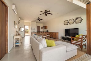 A spacious living area with a sofa, a television, and a dining area with wooden furniture.
