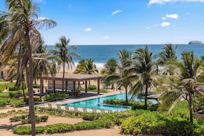 A resort pool area with a view of the ocean, palm trees, and a covered seating area.