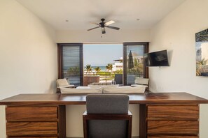 Una habitación con escritorio, dos sillas, ventilador de techo y televisor en la pared.