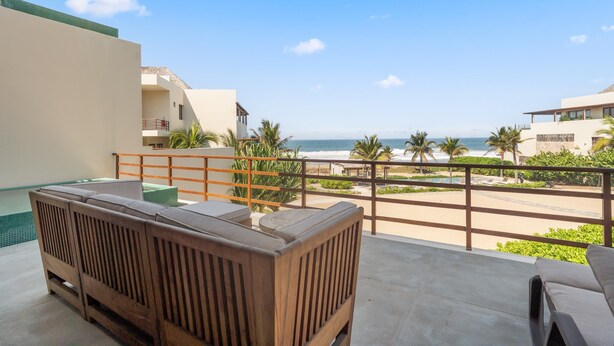 A balcony with a wooden bench, a pool, and a view of the beach and ocean.