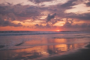 A beach at sunset with waves and clouds.