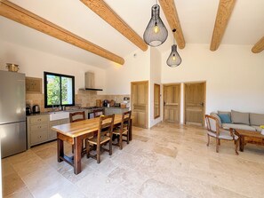 A spacious kitchen with wooden beams, a dining area with a wooden table and chairs, and a living area with a sofa and a coffee table. - Charming 4‑star classified house – Provence, stunning view, private pool (Rustrel)