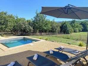 Ein Swimmingpool mit Liegestühlen und einem Sonnenschirm, umgeben von einem Zaun und Bäumen.