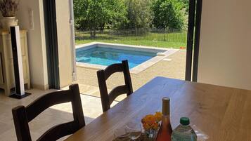 Un espace repas avec vue sur une piscine et un jardin clos.