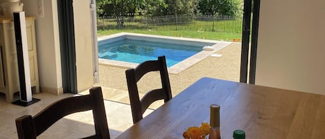 Un espace repas avec vue sur une piscine et un jardin clos.