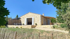 A stone house with a wooden deck, a covered seating area, and a fenced garden.