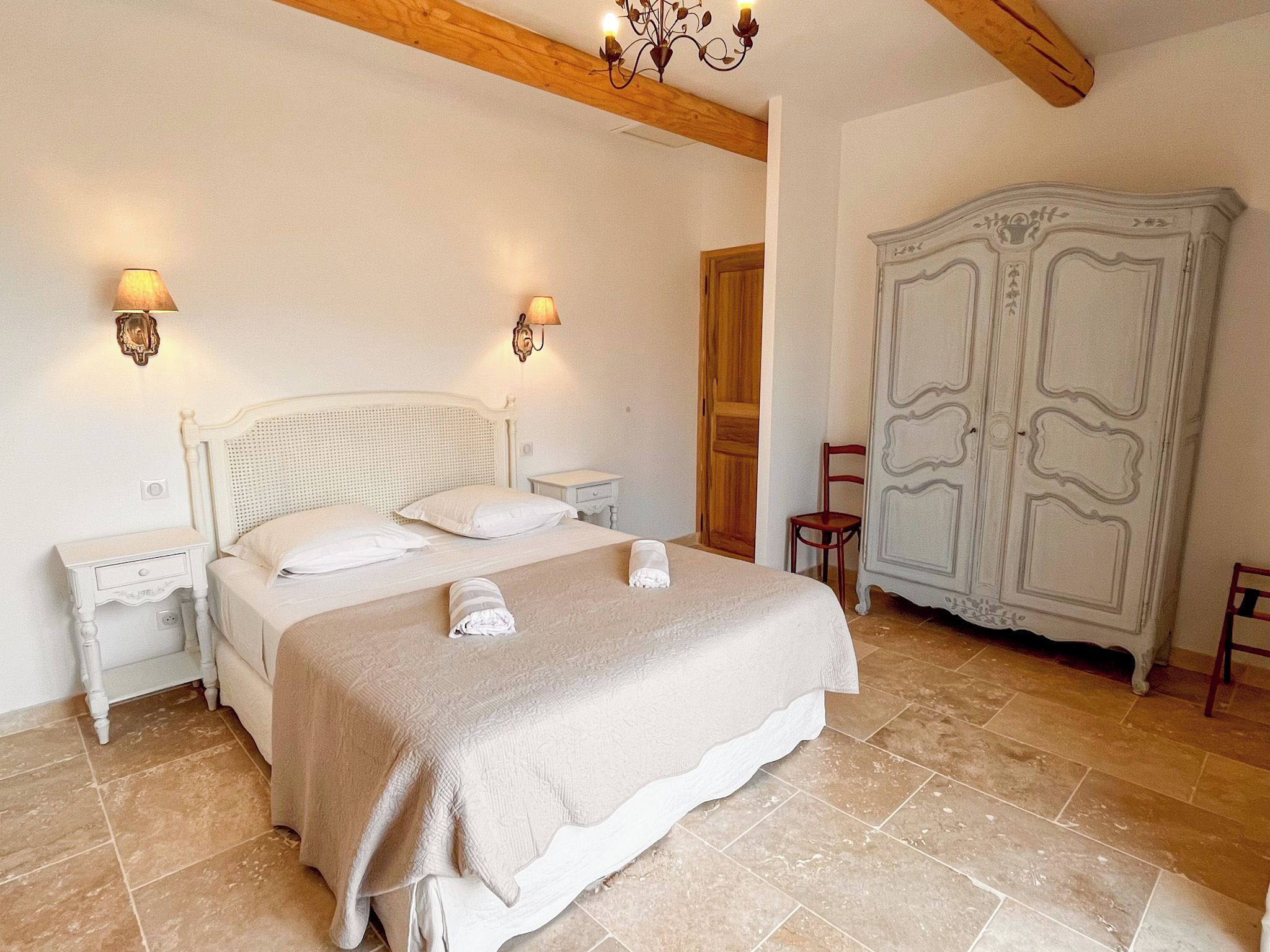 A bedroom with a bed, bedside lamps, a wardrobe, and a chandelier.