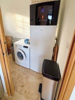 Un espace buanderie compact comprenant un lave-linge Bosch, un réfrigérateur Daik et une poubelle.