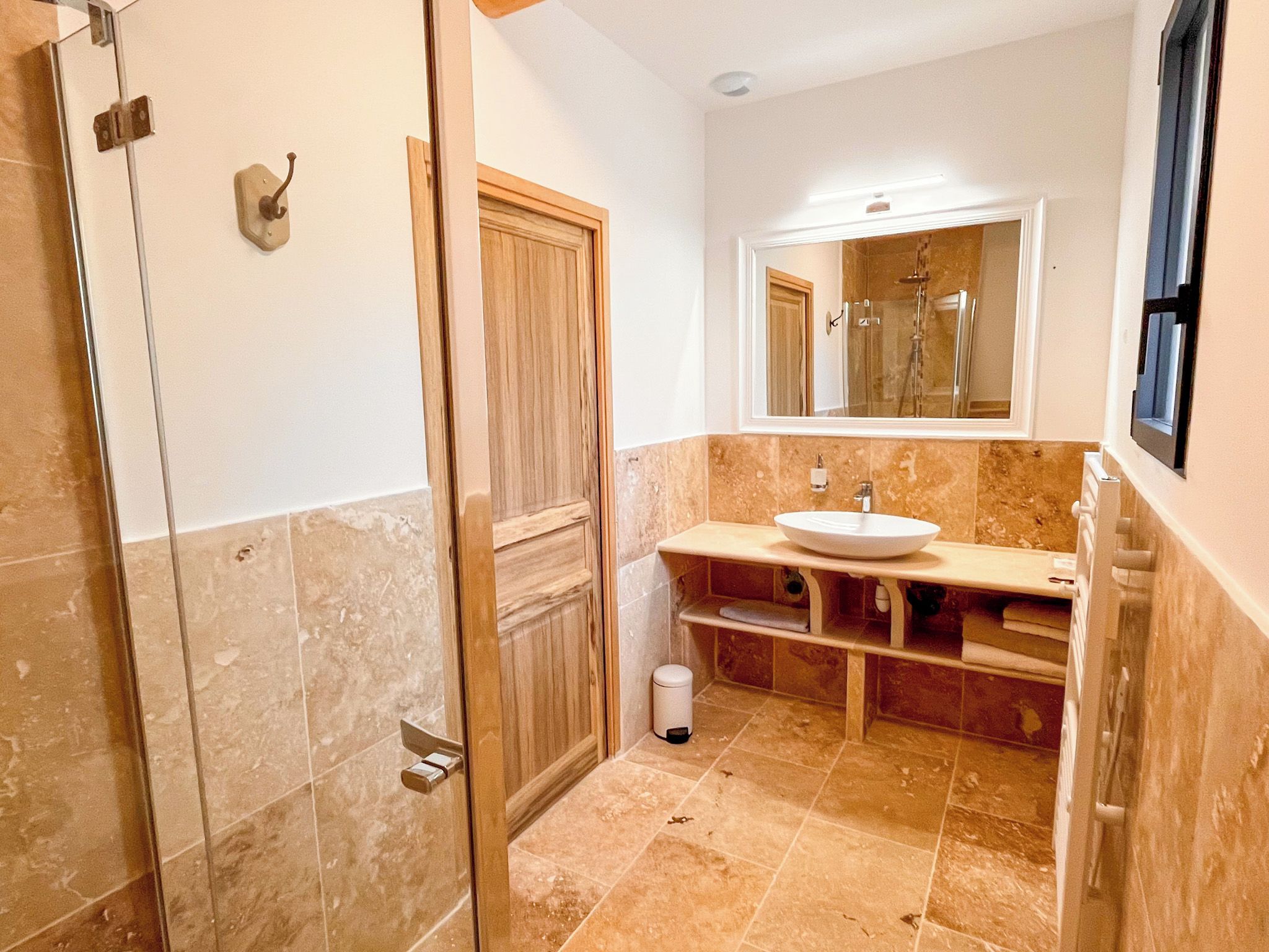 A bathroom with a glass shower enclosure, a sink with a marble countertop, and a mirror above the sink.