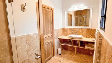 Une salle de bain dotée d’une douche à parois de verre, d’un lavabo avec un plan de travail en marbre et d’un miroir au-dessus du lavabo.