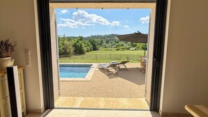 Une porte ouverte donne sur un espace piscine, d’où l’on aperçoit un vignoble et une maison au loin.