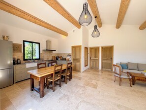 Une cuisine spacieuse avec des poutres en bois, un coin repas avec une table et des chaises, et un salon avec un canapé.