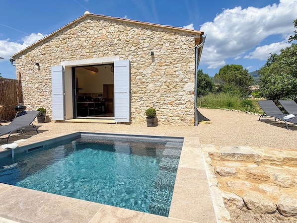 A stone building with a pool, outdoor seating, and a clear sky.